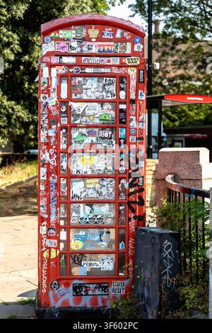 London, England, Vereinigtes Königreich - 17. Juli 2026: Traditionelle rote britische Telefonzelle, bedeckt mit bunten Aufklebern, Graffiti und Street Art Stockfoto