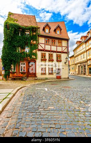 Historische Fachwerkhäuser entlang einer Kopfsteinpflasterstraße in Quedlinburg, Deutschland, mit traditioneller Architektur und einer von Efeu überwucherten Fassade. Stockfoto