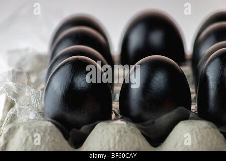 StudienNahaufnahme von schwarz lackierten Eiern in einem Kartoneierkarton, fotografiert aus einem niedrigen Seitenwinkel mit weicher Bokeh-Verwischung der Hintergrundeier. Die l Stockfoto
