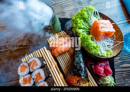Kunstvoll angerichtes Sushi-Sortiment mit geräuchertem Trockeneis-Effekt, frischem Lachs und eleganter japanischer Essenspräsentation. Hochwertiges Foto Stockfoto
