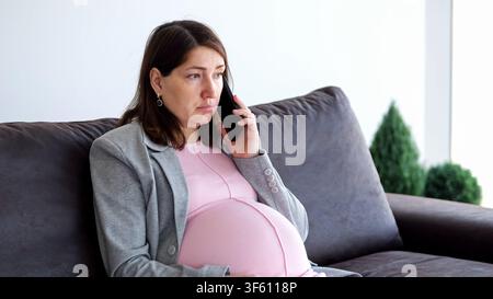 Schwangere Frau führt ein emotionales Telefonat, während sie sitzt Stockfoto