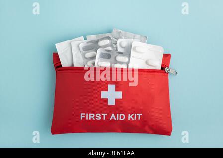 Rotes Erste-Hilfe-Set mit Blisterpackungen mit Pillen und Bandagen vor einem weichen blauen Hintergrund. Saubere helle Beleuchtung, einfache Komposition, nützlich für Stockfoto