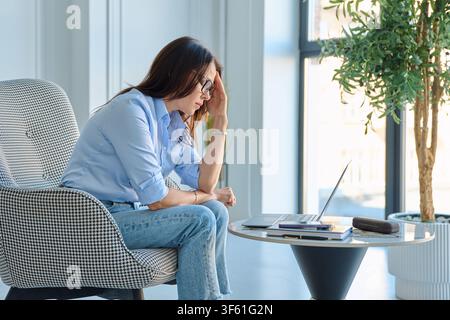 Reife Frau, die unter Hitzewallungen in der Menopause leidet und sich die Stirn bei der Arbeit im Büro abwischt Stockfoto