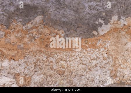 Alte Steinmauer mit abblätternden Schichten, die beige, orange und graue Töne freilegen Stockfoto