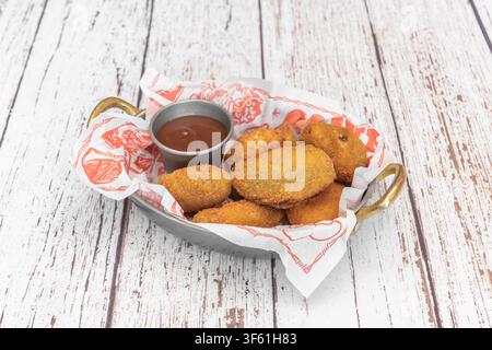 Gebratene Kroketten, serviert in einem Metallkorb mit Dip in einer gemusterten Papierschale Stockfoto