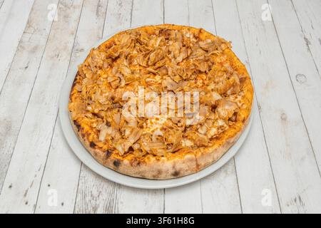 Pizza mit geraspeltem gebratenem Fleisch und Käse auf einem weißen Teller über einem weißen Holztisch. Stockfoto