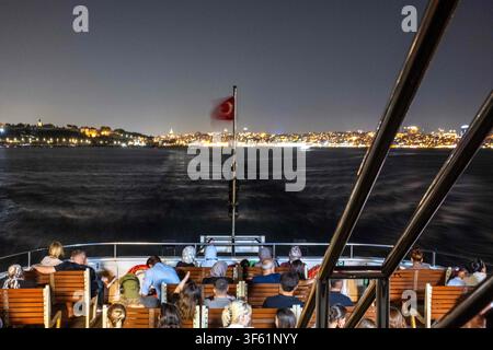 Istanbul, Türkei. 4. Aug., 2026. Menschen sitzen auf dem Deck eines Fährschiffes auf einer nächtlichen Rückfahrt auf die asiatische Seite Istanbuls, Türkei. (Credit Image: © Moe Zoyari/ZUMA Press Wire) NUR FÜR REDAKTIONELLE NUTZUNG! Nicht für kommerzielle NUTZUNG! Stockfoto