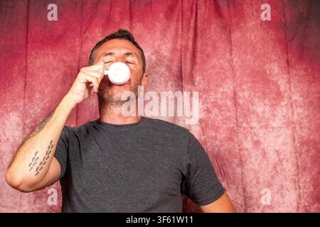 Ein Mann trinkt einen italienischen Kaffee aus einer kleinen weißen Porzellantasse. Der Mann ist zweiundvierzig Jahre alt, hat kurze Haare und einen kurzen Bart Stockfoto