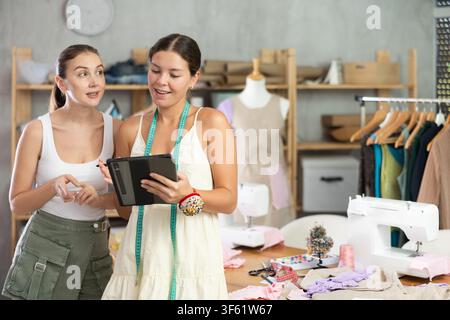 Zwei Schneiderinnen zeichnen ein Modell von Kleidung auf einem Tablet Stockfoto