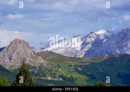 Alpental mit felsigen, schneebedeckten Berggipfeln und grünen Wiesen unter einer bewölkten Himmelsdecke. Stockfoto