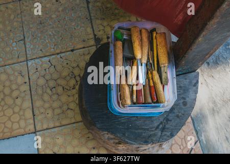 Eine Aufsichtansicht einer Sammlung verschiedener Holzschnitzmeißel und Handwerkzeuge mit abgenutzten Holzgriffen, die in einer klaren Plastikaufbewahrungsbox aufbewahrt werden. Stockfoto