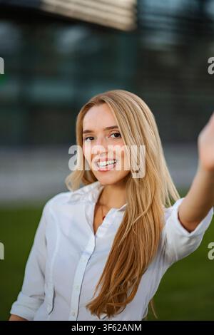 Junge erwachsene Frau lächelt und macht im Freien in der Stadt ein Selfie Stockfoto