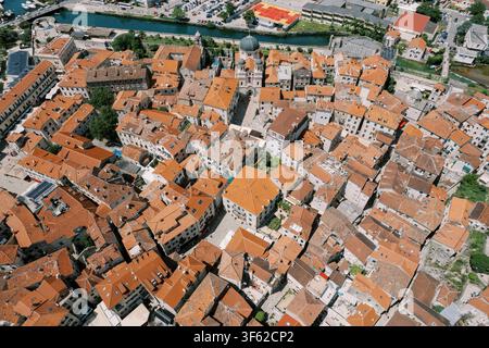 Drohnen-Luftbild der Altstadt von Kotor in Montenegro, das ein dichtes Ensemble historischer Steinbauten mit rotgedeckten Dächern, engen verwinkelten Gassen und der markanten Kuppel der serbisch-orthodoxen Kirche des Heiligen Nikolaus zeigt. Die alte Stadtmauer und ein Riv Stockfoto