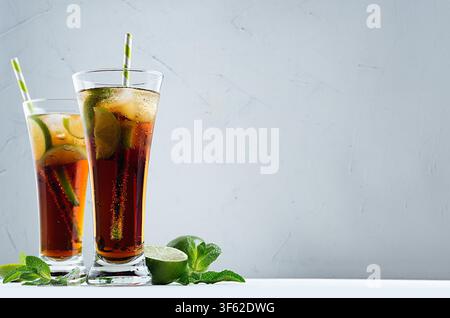 Heller, frischer Cocktail aus Cola mit Eis in zwei Gläsern mit Minze und Limette in dunkelgrauem, modernem Interieur. Stockfoto