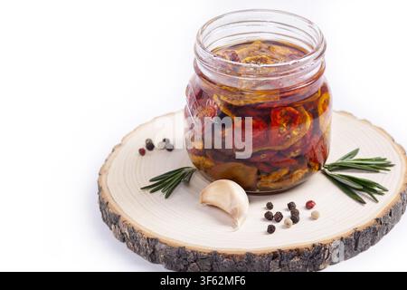 Bunte getrocknete Kirschtomaten verschiedener Sorten (gelb, rot, schwarz) sind in Olivenöl mit Kräutern (Rosmarin, Pfefferkörnern und Knoblauch) eingelegt Stockfoto