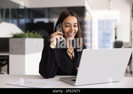 Lächelnde Geschäftsfrau telefoniert, während sie an einem Laptop arbeitet Stockfoto