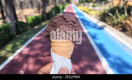Person hält eine Schokoladeneiswaffel auf dem Weg Stockfoto