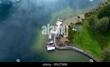 Luftaufnahme zeigt den Uferbereich des Pliva-Sees mit einem Pier, mehreren Booten, Kajaks und einem geschwungenen Promenadenweg entlang des grünen Grases Stockfoto