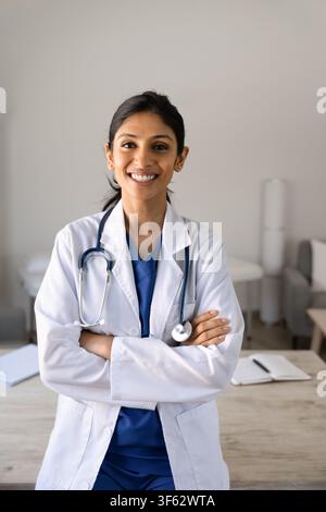 Lächelnde südasiatische Ärztin im Kittel, die in einer Klinik steht Stockfoto