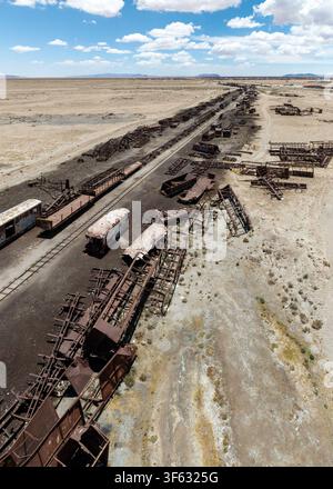 Luftaufnahme des historischen Zugfriedhofs mit verlassenen, verrosteten Lokomotiven und Waggons, die über die trockene Wüstenlandschaft in Bolivien verstreut sind. Stockfoto