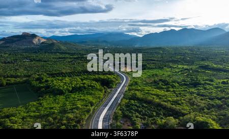 Drohnenperspektive einer asphaltierten Autobahn, die sich durch eine üppige Waldlandschaft zur Bergkette windet Stockfoto