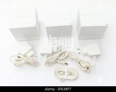 Drei weiße würfelförmige Mesh-Router werden zusammen mit ihren entsprechenden Netzteilen und Kabeln auf einer weißen Oberfläche angezeigt Stockfoto