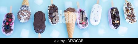 Bunte Runde aus hausgemachtem Joghurt- und Milch-Eis am Stiel. Vanille und Schokolade, verziert mit Nüssen und gefrorenen Beeren auf hellem blauem Hintergrund. Perfekt für eine sommerliche Kindergeburtstagsfeier. Stockfoto