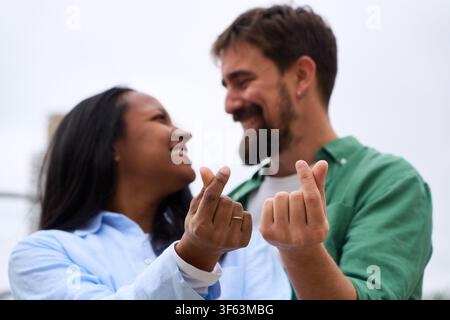 Mischhautfarben-Paar macht ein koreanisches Fingerherzzeichen, während sie sich gegenseitig anschauen. Stockfoto