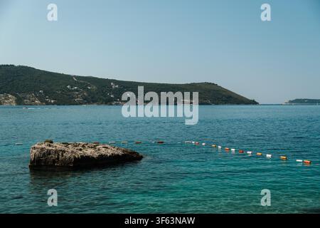 Weite Küstenlandschaft mit ruhigem blauem Wasser und fernen grünen Hügeln. Friedliches Meerespanorama bei klarem Sommerwetter. Stockfoto