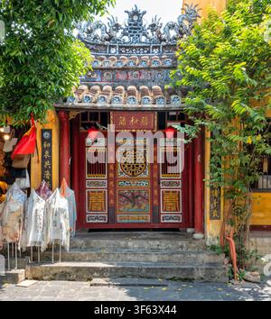 Historische Fassade mit kunstvollen roten Holztüren und Laternen an einem traditionellen Gebäude in der Altstadt von Hoi An, Vietnam, mit Seidenschals, die auf th Stockfoto