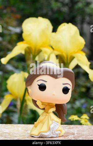 Funko-Pop-Actionfigur der Disney-Prinzessin Belle aus dem Animationsfilm Die Schöne und das Biest. Puppe steht vor gelben Schwertlilien. Stockfoto