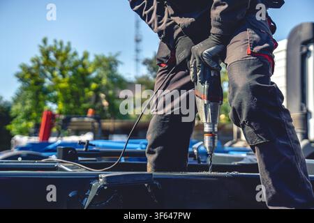 Nahaufnahme eines Arbeiters, der einen Akku-Bohrer verwendet, um ein Loch in einen schweren Metallstahlrahmen im Freien zu bohren, Konzept für Bau und Handarbeit Stockfoto