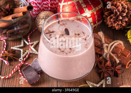 Gewürzter Schokoladen-Eierlikör-Punsch-Cocktail, serviert mit Zimtstab, Muskatnuss und Schokolade, auf gemütlichem Weihnachtshintergrund Stockfoto