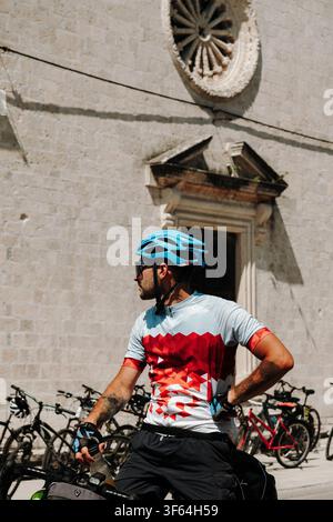 Nahaufnahme eines Radfahrers neben einer historischen Kirche in Prcanj an der Bucht von Kotor. Sommerradtour durch die mediterrane Küste Montenegros. Stockfoto