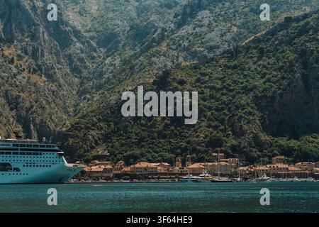 Kreuzfahrtschiff passiert die Bucht von Kotor unter hoch aufragenden Bergen. Malerische Adrialandschaft in Montenegro während der Sommersaison. Stockfoto