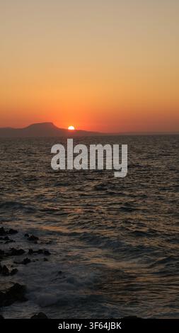 Die Sonne sinkt kurz vor dem Untergang hinter dem Meereshorizont über dem Strand in Rethymno, Kreta, Griechenland. Stockfoto
