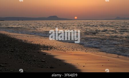 Die Sonne sinkt kurz vor dem Untergang hinter dem Meereshorizont über dem Strand in Rethymno, Kreta, Griechenland. Stockfoto