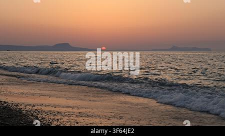 Die Sonne sinkt kurz vor dem Untergang hinter dem Meereshorizont über dem Strand in Rethymno, Kreta, Griechenland. Stockfoto