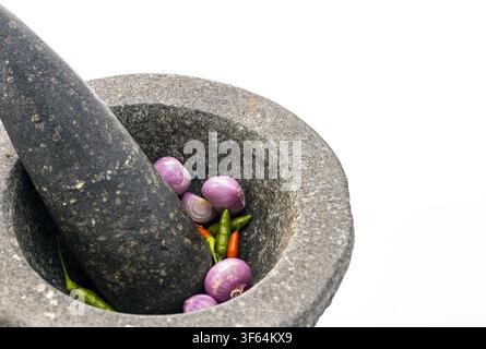 Traditioneller Granitstein-Mörser und Stößel mit frischen violetten Schalotten und roten grünen Chilischoten, authentisches thailändisches Küchenwerkzeug für Currypaste Stockfoto