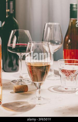 Verschiedene Weinarten werden in Gläsern zusammen mit Weinflaschen auf einem Tisch serviert. Ein Korken liegt in der Nähe. Die Umgebung wirkt einladend und entspannt Stockfoto