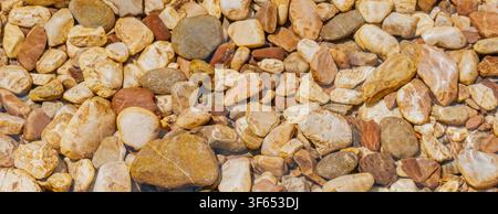 Oberblick abstrakter Hintergrund aus glatten Flusssteinen und Kieselsteinen unter klarem flachem Wasser mit Lichtkaustiken für natürliches Spa- und Entspannungs-Hintergrundbild Stockfoto