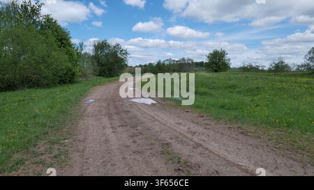 Schmutzige Schotterstraße mit Pfützen in einer ländlichen Landschaft Stockfoto