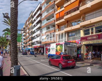 Ein rotes Auto steht an einer belebten Straße, die mit mehrstöckigen Gebäuden und Palmen gesäumt ist. Fußgänger gehen auf den Gehwegen. Stockfoto