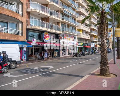 Eine Straßenszene vor einem Burger-King-Restaurant, mit Menschen, die in der Nähe des Eingangs gehen. Mehrere Roller sind am Gehweg geparkt. Stockfoto