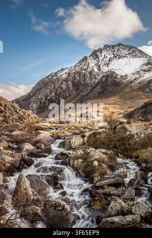 Ein felsiger Gebirgsbach stürzt über Geröll die Hänge von Pen yr Ole Wen hinab, mit Blick auf den schneebedeckten Gipfel des Tryfan in Nordwales. Reisen Stockfoto