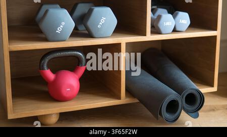 Ordentlich organisierte Home-Gym-Ausrüstung mit Hanteln, rotem Kettlebell und gerollten Yogamatten auf Eichenregalen — Home Fitness, Wellness und Innenraumaufbewahrung Stockfoto