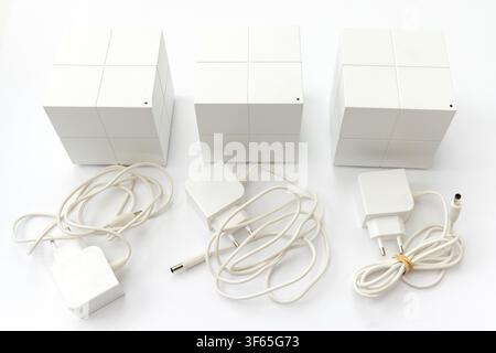 Drei weiße Mesh-WLAN-Router-Einheiten sind mit ihren jeweiligen Stromadaptern und Kabeln auf einer weißen Oberfläche angeordnet Stockfoto