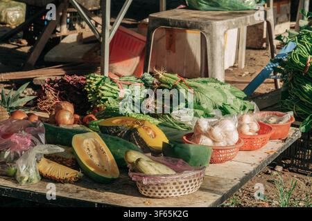 Eine große Vielfalt an frischem Gemüse und Obst, darunter Kürbis, Papaya, Grünzeug und Zwiebeln, ist auf einem Holztisch an einem Marktstand unter freiem Himmel angeordnet Stockfoto