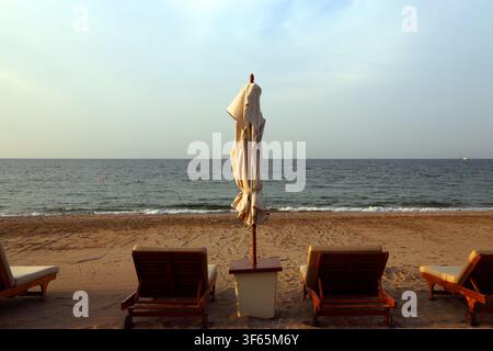 Leere Sonnenliegen und geschlossener Sonnenschirm am Strand am Abend im The Chedi Hotel Muscat Oman Stockfoto