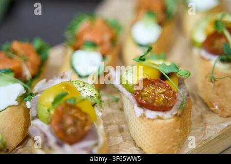 Verschiedene Bruschetta mit Tomaten, Avocado-Creme und Mikrogrün, angeordnet auf einem Holzbrett als Vorspeisenpräsentation bei einer Catering-Veranstaltung. Stockfoto